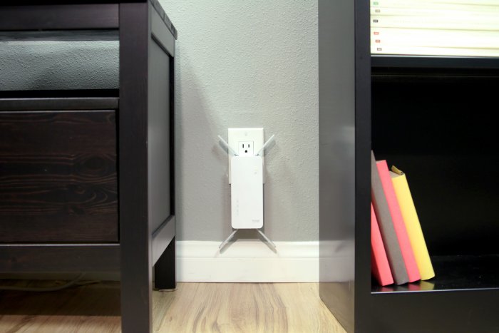 D-Link AC2600 Wi-Fi range extender (DAP-1860) plugged into a wall outlet between a bookcase and an entertainment center.